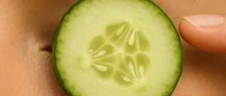 Close-up of a woman's right eye with a fresh cucumber slice placed on it to reduce puffiness naturally