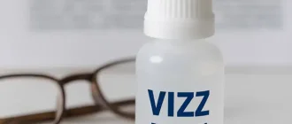 VIZZ eye drops bottle with reading glasses on blurred text, symbolizing presbyopia treatment and clear near vision.